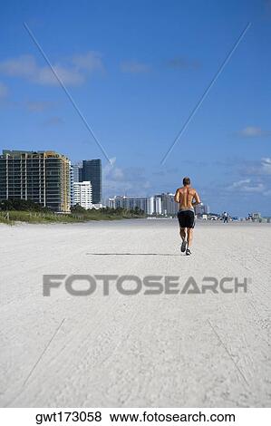 Stock Photo - Rear view of a man jogging on the beach, South Beach, Miami Beach, Florida, USA. Fotosearch