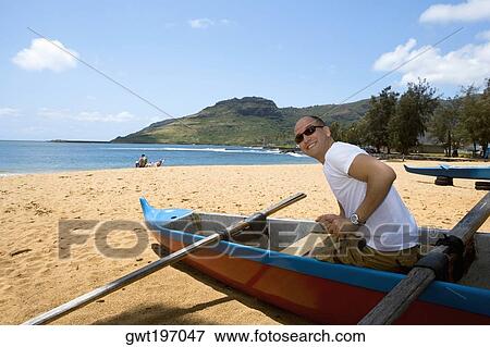 Stock Photo - Side profile of a mid adult man sitting in a boat on the beach, Nawiliwili Beach Park, Kauai, Hawaii Islands, USA. Fotosearch