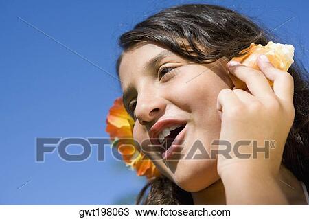 Stock Image - Close-up of a girl wearing flowers and listening to a conch shell. Fotosearch