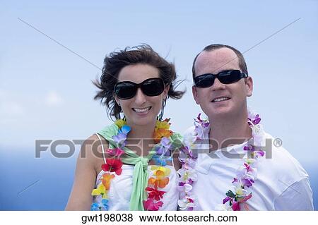 Stock Photo - Mid adult couple wearing garlands and smiling. Fotosearch