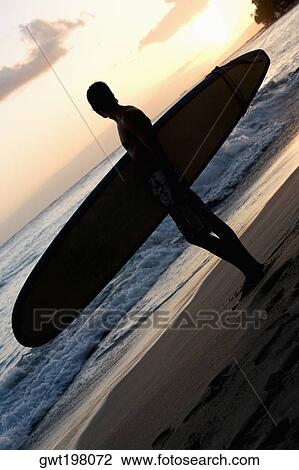 Silhouette of a man holding a surfboard and standing on the beach, Waikiki Beach, Honolulu, Oahu, Hawaii Islands, USA View Large Photo Image Stock Image - Silhouette of a man holding a surfboard and standing on the beach, Waikiki Beach, Honolulu, Oahu, Hawaii Islands, USA. Fotosearch