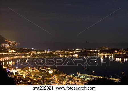 Stock Image - High angle view of buildings lit up at night near a harbor, Nice, France. Fotosearch