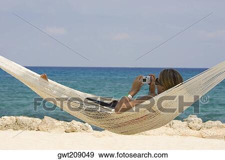 Young woman lying in a hammock and holding a digital camera, Cancun, Mexico View Large Photo Image Stock Photo - Young woman lying in a hammock and holding a digital camera, Cancun, Mexico. Fotosearch