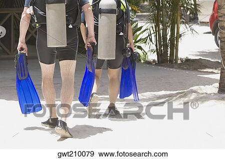 Stock Photo - Rear view of two scuba divers walking on the beach, Honduras. Fotosearch