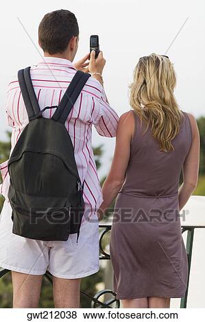 Rear view of a mid adult couple taking photographs with a mobile phone, Capri, campania, Italy View Large Photo Image Stock Photo - Rear view of a mid adult couple taking photographs with a mobile phone, Capri, campania, Italy. Fotosearch
