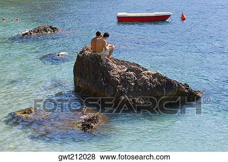 Stock Photo - Tourists sitting on a rock, Capri, Campania, Italy. Fotosearch