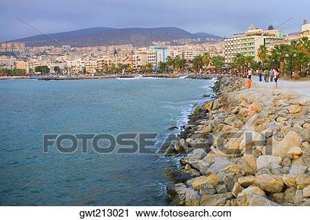 Stock Image - Tourists sitting on rocks at the coast, Ephesus, Turkey. Fotosearch