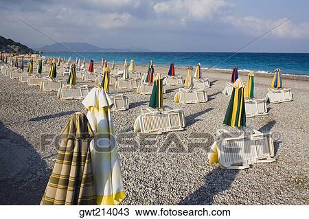 Stock Image - Beach umbrellas and lounge chairs on the beach, Rhodes, Dodecanese Islands, Greece. Fotosearch