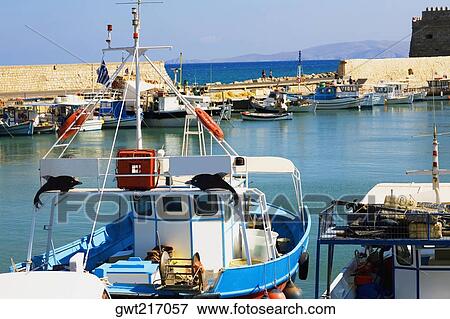 Stock Photo - Boat at a harbor with a fortress in the background, Venetian Fortress, Heraklion Harbour, Heraklion, Crete, Greece. Fotosearch