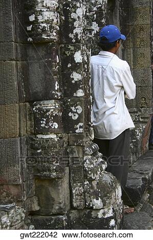 Stock Image - Rear view of a mid adult man leaning against a wall, Ta Prohm Temple, Angkor Wat, Siem Reap, Cambodia. Fotosearch