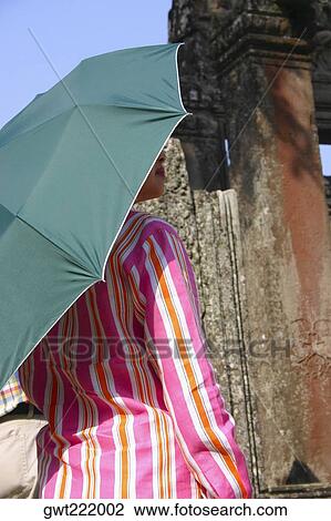 Stock Image - Rear view of a woman under an umbrella in a temple, Ta Prohm Temple, Angkor Wat, Siem Reap, Cambodia. Fotosearch
