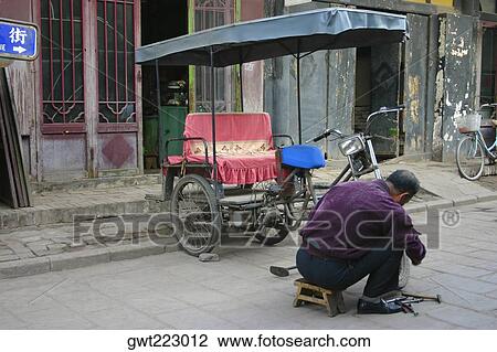 Stock Image - Rear view of a mechanic repairing a pedicab, Pingyao, Shaanxi Province, China. Fotosearch