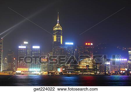 Stock Image - Skyscrapers lit up at night in a city, Victoria Harbor, Hong Kong Island, Hong Kong, China. Fotosearch