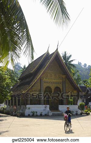 Picture - Girl riding a bicycle in front of a temple, Wat Si Amphon, Vientiane, Laos. Fotosearch