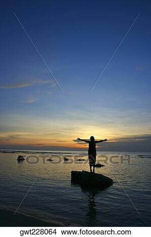Silhouette of a woman standing on a stone with her arms outstretched in the sea, Thailand View Large Photo Image Picture - Silhouette of a woman standing on a stone with her arms outstretched in the sea, Thailand. Fotosearch
