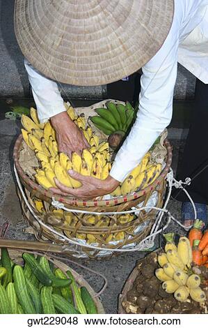 Stock Photo - High angle view of a man arranging bananas in a basket, Hanoi, Vietnam. Fotosearch