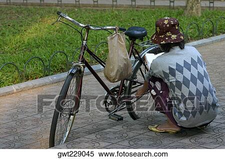 Stock Photography - Rear view of a woman repairing a bicycle, Hanoi, Vietnam. Fotosearch