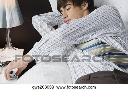 Stock Photo - Close-up of a businessman lying on the bed and holding a mobile phone. Fotosearch