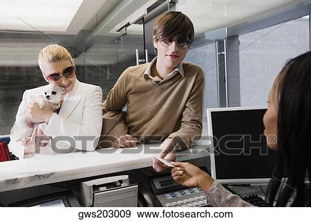 Young man giving a credit card to the receptionist View Large Photo Image Stock Photo - Young man giving a credit card to the receptionist. Fotosearch
