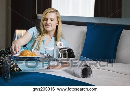 Stock Photograph - Young woman having breakfast on the bed. Fotosearch