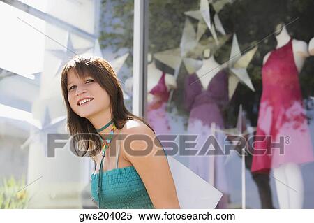 Side profile of a young woman carrying a shopping bag in front of a clothing store View Large Photo Image Stock Photography - Side profile of a young woman carrying a shopping bag in front of a clothing store. Fotosearch