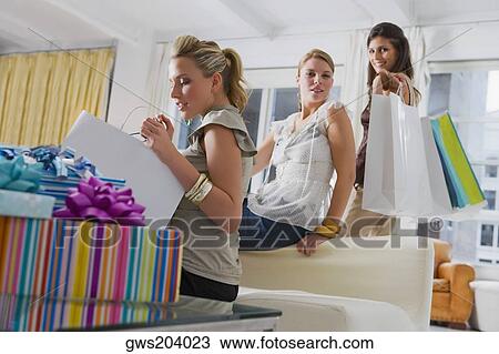 Young woman checking her shopping bags with her friends in the background View Large Photo Image Stock Image - Young woman checking her shopping bags with her friends in the background. Fotosearch