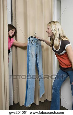 Young woman taking jeans from a sales clerk in a fitting room View Large Photo Image Stock Image - Young woman taking jeans from a sales clerk in a fitting room. Fotosearch