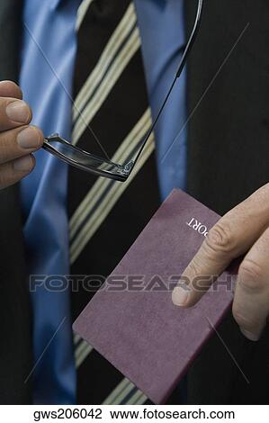 Stock Image - Close-up of a man's hands holding a passport and eyeglasses. Fotosearch