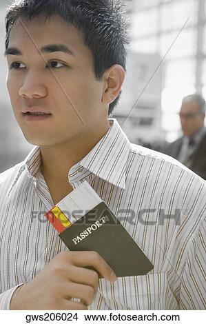 Picture - Close-up of a young man putting a passport with an airplane ticket in his shirt's pocket. Fotosearch