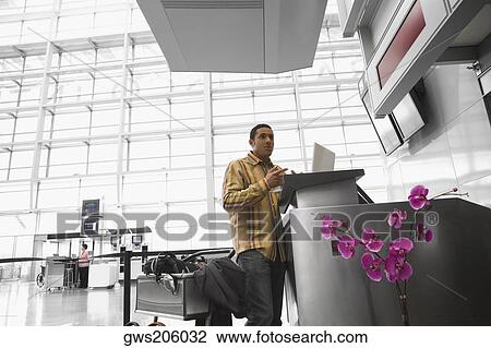 Stock Image - Low angle view of a mid adult man using a laptop at an airport. Fotosearch