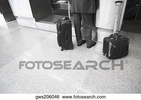 Stock Photograph - Low section view of a businessman standing with his luggage at an airport. Fotosearch