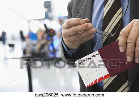 Stock Photography - Mid section view of a businessman holding eyeglasses and a passport with an airplane ticket. Fotosearch