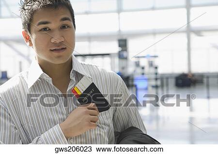 Stock Image - Portrait of a young man putting a passport with an airplane ticket in his shirt's pocket. Fotosearch