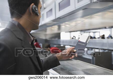 Picture - Side profile of a businessman holding a passport with an airplane ticket at an airport. Fotosearch