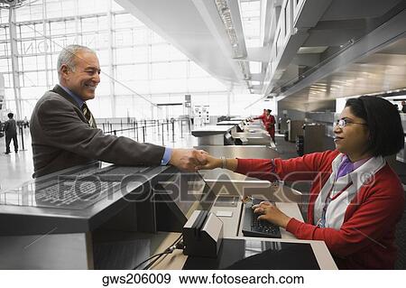 Stock Photo - Side profile of a businessman shaking hands with an airline check-in attendant and smiling. Fotosearch