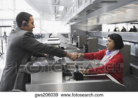 Stock Photo - Side profile of a businessman shaking hands with an airline check-in attendant. Fotosearch