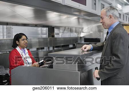 Stock Image - Side profile of a businessman standing at a ticket counter in an airport. Fotosearch