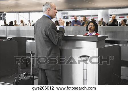 Stock Image - Side profile of a businessman standing at a ticket counter in an airport. Fotosearch