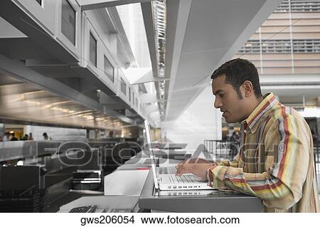 Picture - Side profile of a mid adult man using a laptop at an airport. Fotosearch