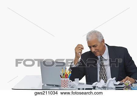 Businessman sitting at a desk with crumpled paper on the desk View Large Photo Image Picture - Businessman sitting at a desk with crumpled paper on the desk. Fotosearch