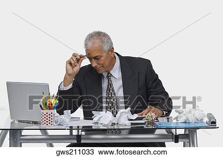 Stock Image - Businessman sitting at a desk with crumpled papers on the desk. Fotosearch