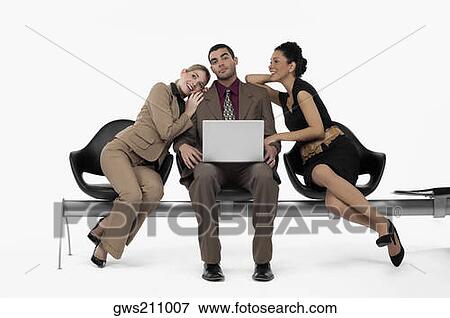 Stock Photo - Businessman using a laptop and two businesswomen leaning on his shoulders. Fotosearch