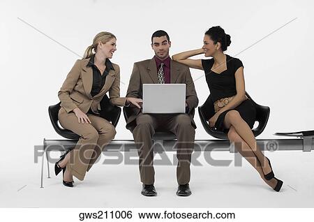 Businessman using a laptop and two businesswomen sitting beside him View Large Photo Image Stock Photograph - Businessman using a laptop and two businesswomen sitting beside him. Fotosearch