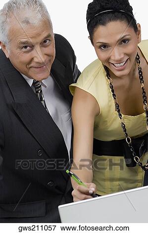 Portrait of a businesswoman and a businessman discussing on a laptop in an office and smiling View Large Photo Image Stock Photo - Portrait of a businesswoman and a businessman discussing on a laptop in an office and smiling. Fotosearch