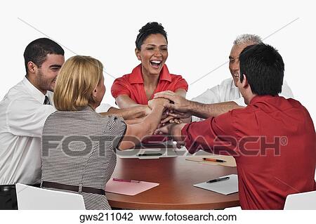 Stock Image - Three businessmen and two businesswomen stacking hands on top of each other in a meeting. Fotosearch