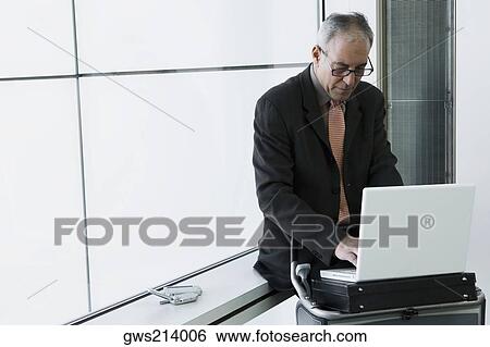 Businessman using a laptop in the waiting room of an airport View Large Photo Image Stock Photograph - Businessman using a laptop in the waiting room of an airport. Fotosearch