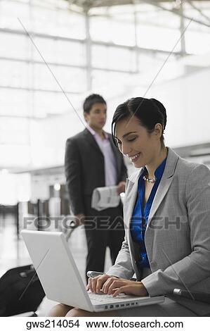 Businesswoman using a laptop and a businessman pulling his luggage behind her View Large Photo Image Picture - Businesswoman using a laptop and a businessman pulling his luggage behind her. Fotosearch