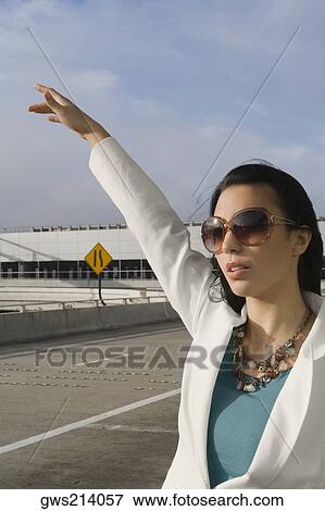 Stock Photo - Close-up of a businesswoman hailing a taxi outside an airport. Fotosearch