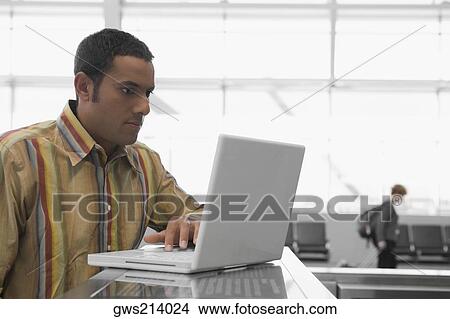 Mid adult man using a laptop at an airport and looking serious View Large Photo Image Picture - Mid adult man using a laptop at an airport and looking serious. Fotosearch