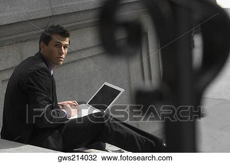 Stock Image - Portrait of a businessman sitting on steps and using a laptop. Fotosearch